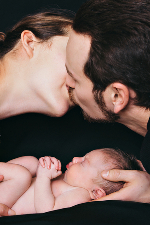 newborn baby lying on the hands of parents on a black background.の写真素材