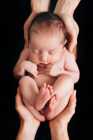 newborn baby lying on the hands of parents on a black background. Imitation of a baby in the womb.の写真素材
