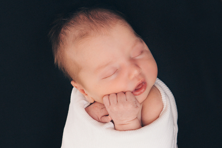 newborn baby sleeping wrapped in white scarf on black backgroundの写真素材