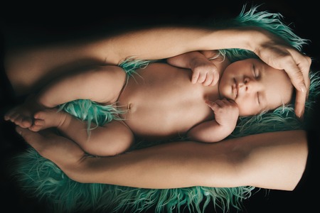 Newborn baby lying in the hands of parents on a green background.の写真素材