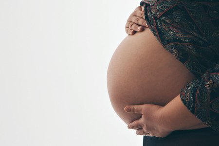 pregnant woman holding hands on belly on a white backgroundの写真素材