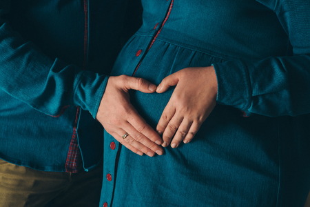 pregnant woman and man holding hands heart shaped on belly on a white backgroundの写真素材