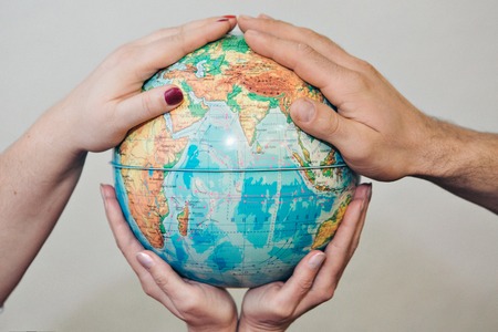 Four hands holding globe on white background. The globe is in the palmの写真素材