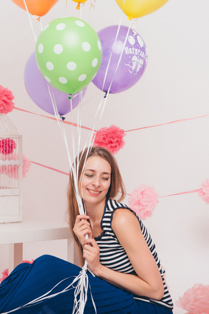 The blonde smiles and looks at the camera between the coloured balls on a white background.の写真素材