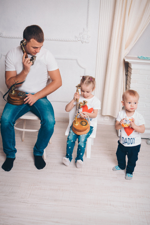 family portrait: father and two children. Business situation: telephone conversations. A man, a boy, a girl sit in a lineの写真素材