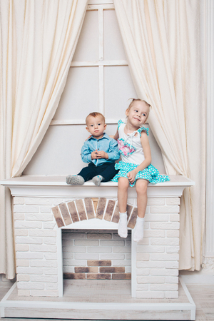 a little girl and a guy in a dress sitting by the fireplace. Family portrait: sister and brotherの写真素材