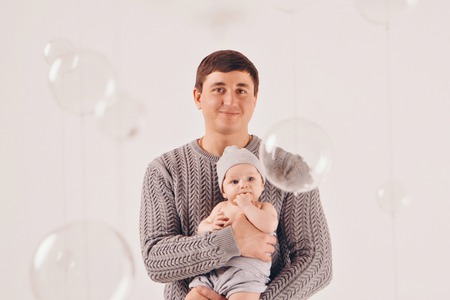 portrait: happy dad holds a child in a knitted hat in his hands. Family in warm grey clothes on...