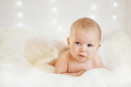 a blue-eyed boy with his mouth open is lying on his stomach on a white background with wings behind his back. Angel Cupid looks upの写真素材