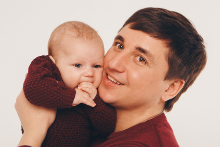 portrait: happy dad holds a child in a knitted hat in his hands. Family in warm grey clothes on white backgroundの写真素材