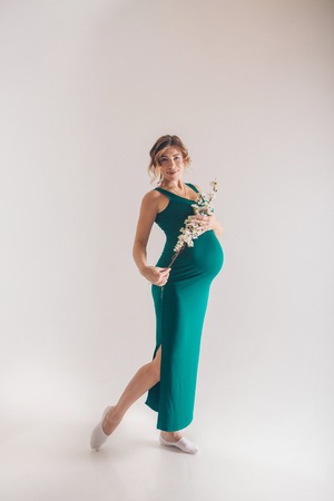 pregnant ballerina dancing on a white background. Future mother in a green dress posingの写真素材