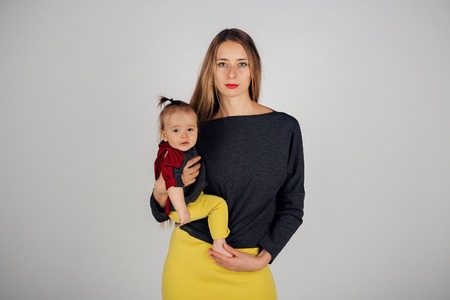 family photo: a woman holding a child in her arms. Fashion for the whole family: mother and daughter dressed in yellow-gray. Model shows clothesの写真素材