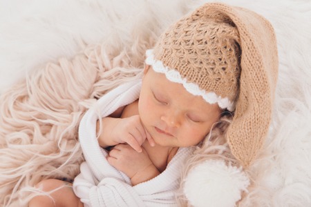 A small child in a beige knitted hat with a pompom folded his hands and sleepingの写真素材