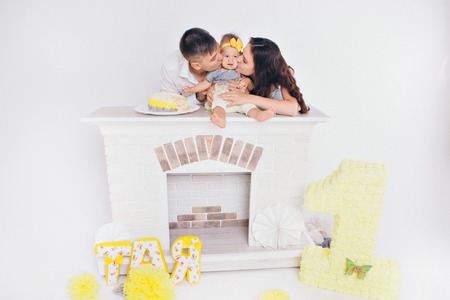 Parents hold the child in their arms between them, sitting on the fireplace and kiss the child. Man, woman and son daughter on white backgroundの写真素材