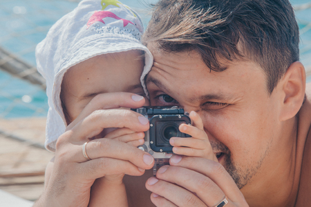 A man takes a little child with a camera in her hands on a lake background.の写真素材