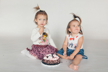Two little baby girl eating cake isolated white backgroundの写真素材