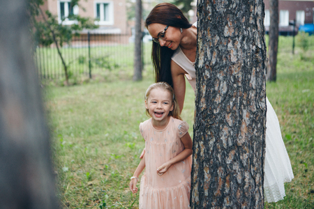 mom and daughter are hiding behind a tree. a woman and a little girl peeking out from behind a pine treeの写真素材
