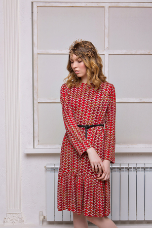 beautiful girl model stands in a red dress by the window on a white backgroundの写真素材