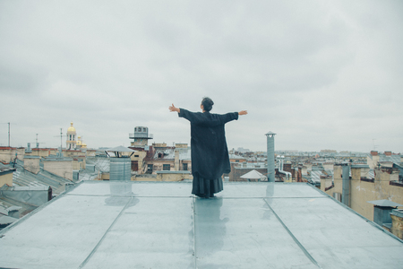 girl in black clothes standing on the edge of the roof, arms outstretchedの写真素材