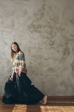 the model advertises a beige shirt with a free cut with flowers and wide black pants in Japanese style. Beautiful girl posing against a concrete wallの写真素材