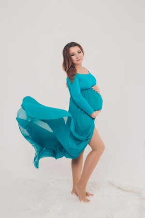 Isolated photo on a white background: a beautiful pregnant woman in a blue dress put her hands on her stomachの写真素材