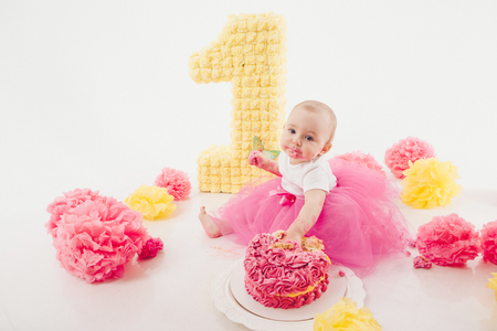a little girl eats cake with her hands. The baby was covered in food. isolated white background. birthday partyの写真素材