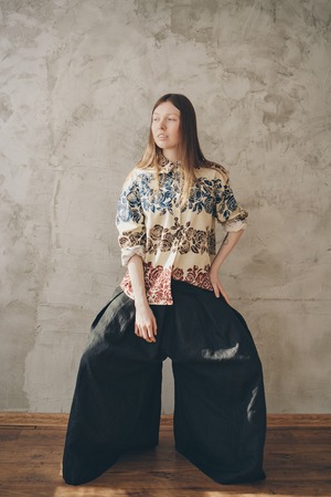the model advertises a beige shirt with a free cut with flowers and wide black pants in Japanese style. Beautiful girl posing against a concrete wallの写真素材