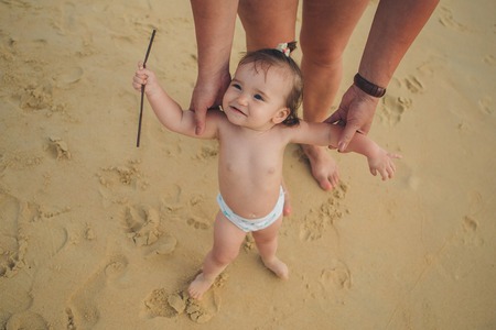 a small child learns to walk, holding the hand of parents on the sea coastの写真素材