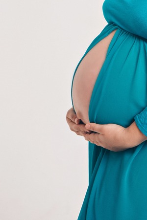 Isolated photo on a white background: a beautiful pregnant woman in a blue dress put her hands on her stomachの写真素材