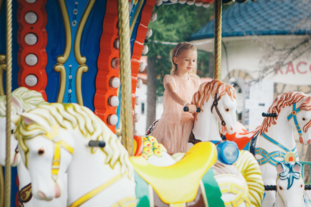 little girl riding in the Park on a toy horse on the carouselの写真素材