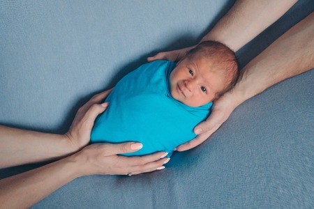 portrait of newborn baby lying on the hands of parents on a blue backgroundの写真素材