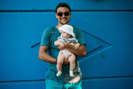 Dad holds the baby in his arms. The concept of educating the father of young children, Happy childhood, a friendly family. Isolated on blue background.の写真素材