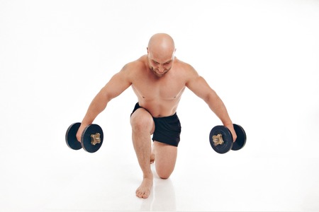 the naked muscular man lifts heavy dumbbellsの写真素材