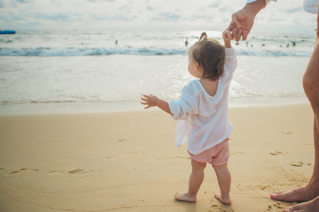 a small child learns to walk, holding the hand of parents on the sea coastの写真素材