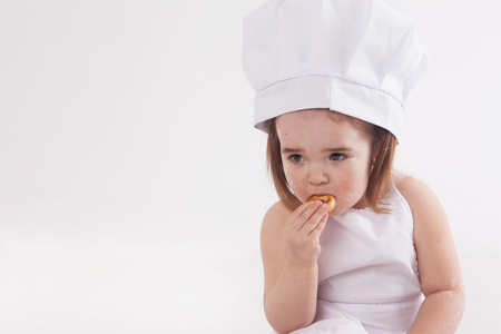 Portrait of a little girl in a white cap and covered in flour face eating dried on white backgroundの写真素材
