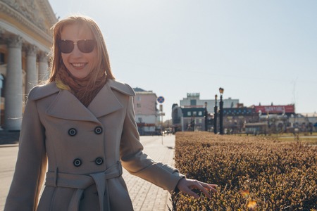 portrait of a beautiful blonde in a coat and sunglasses on the background of the city landscape in the cold season. girl walking down the streetの写真素材