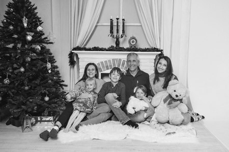 a group of 7 people and one Teddy: a large family sitting on the floor against the fireplace, Christmas decorations, Christmas trees, clocks, candelabraの写真素材