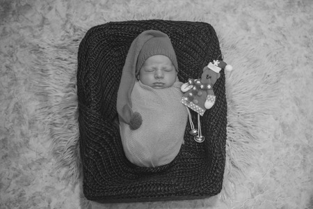a newborn baby sleeps in a basket in an orange hat with a POM-POM, like a gnome, and with a Christmas toyの写真素材