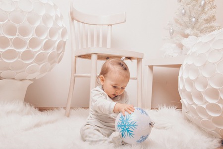a small child sitting on the floor with a Christmas ball in his hands among the white furnitureの写真素材