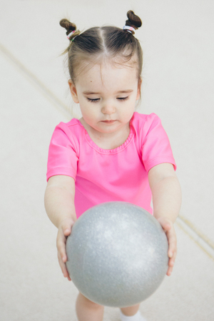 a little girl in a pink swimsuit doing gymnastics with a small ballの写真素材