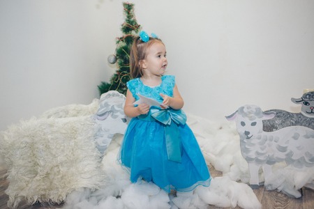 a little girl in a blue dress celebrates the new year: a child among the snow of cotton wool, painted sheep, Christmas tree and starsの写真素材