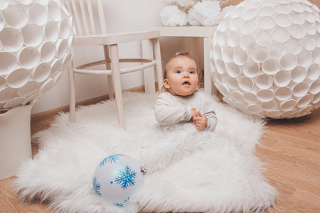 a small child sitting on the floor with a Christmas ball in his hands among the white furnitureの写真素材