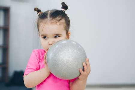 a little girl in a pink swimsuit doing gymnastics with a small ballの写真素材