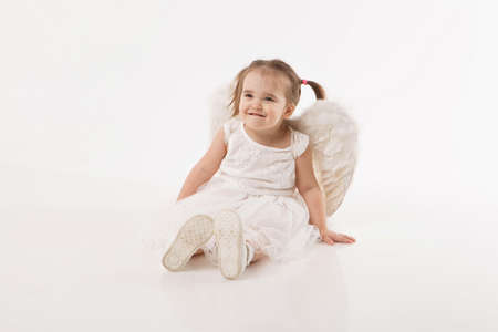 little girl in white dress with wings playing on white backgroundの写真素材