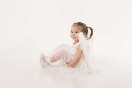 little girl in white dress with wings playing on white backgroundの写真素材
