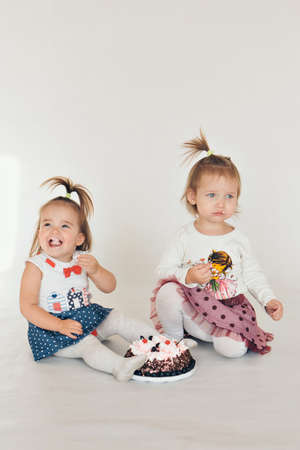 Two little baby girl eating cake isolated white backgroundの写真素材