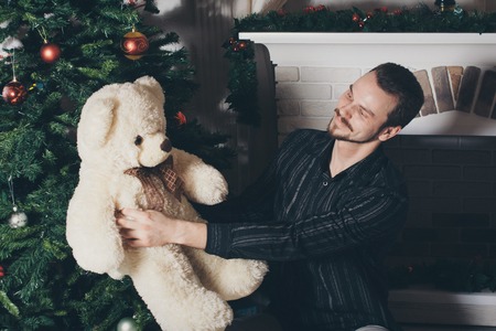 handsome man with a Teddy bear on the background of Christmas attributes: fireplace, Christmas tree, Christmas decorationsの写真素材
