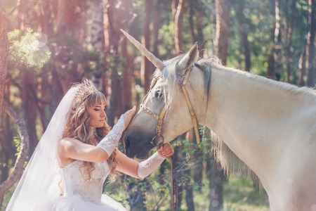 bride stroking the white unicorn on the forest backgroundの写真素材