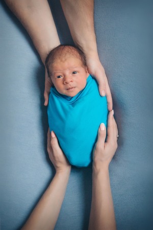 portrait of newborn baby lying on the hands of parents on a blue backgroundの写真素材