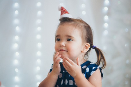 portrait of a little girl in a red Christmas cap on the background of lightsの写真素材
