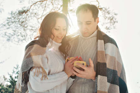 man and woman wrapped in a blanket and holding cups in the background of winter forestの写真素材